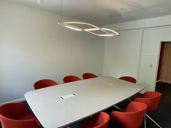 Salle de réunion aménagée avec table blanche, fauteuils rouges et éclairage LED suspendu