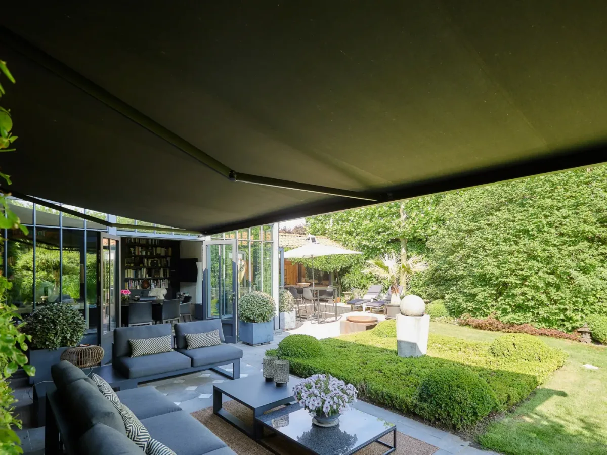 Banne solaire anthracite déployée au-dessus d’un salon de jardin donnant sur un jardin paysager