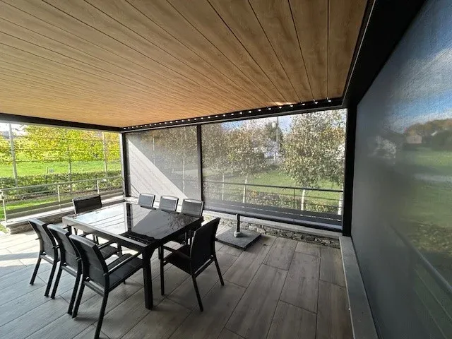 Terrasse couverte à plafond en bois, spots encastrés et screens descendus, avec table et chaises de jardin