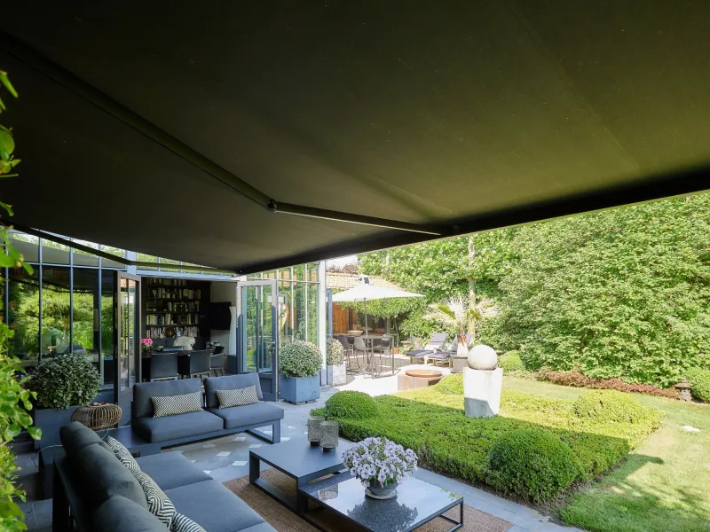 Banne solaire anthracite déployée au-dessus d’un salon de jardin donnant sur un jardin paysager