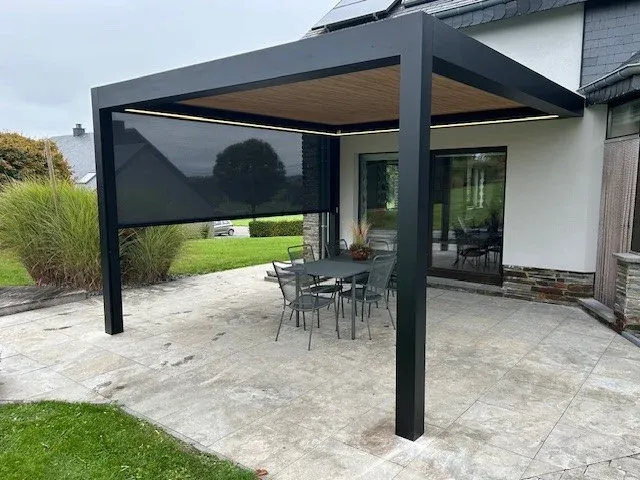 Pergola bioclimatique anthracite à plafond bois adossée à une maison, avec table et chaises de jardin