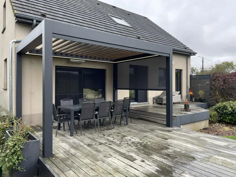 Pergola bioclimatique anthracite au-dessus d’une terrasse en bois, avec table et chaises de jardin