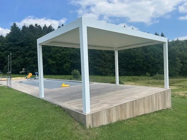 Pergola bioclimatique blanche sur une terrasse en bois, au bord d’une piscine