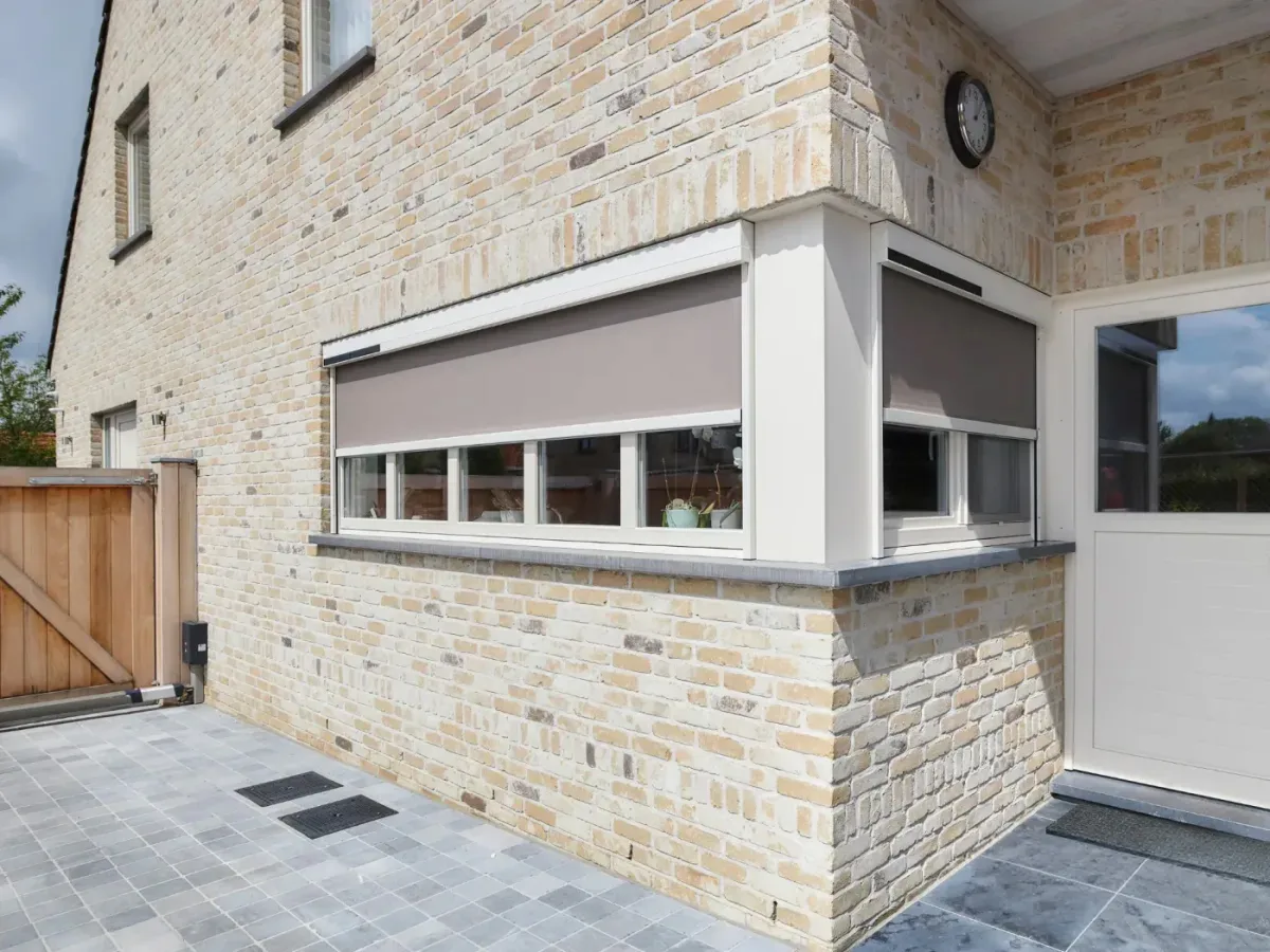 Screens gris descendus sur les fenêtres d’angle d’une maison en briques claires
